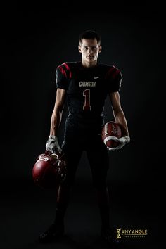 a football player is holding his helmet and ball while posing for a photo in the dark