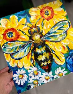 a painting of a bee and sunflowers on a piece of paper with a person's hand holding it