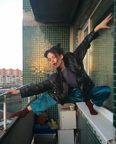 a man in black jacket and blue pants standing on top of a building with his arms out