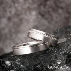 two wedding rings sitting on top of a rock next to each other with white diamonds