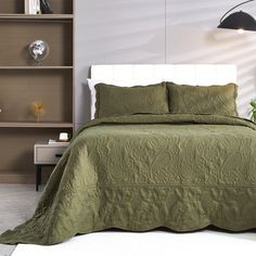 a bed with green bedspread and pillows in a room next to a bookcase