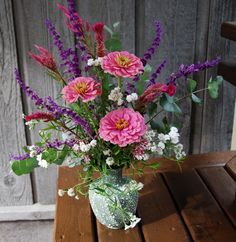 a vase filled with pink and purple flowers on top of a wooden table next to a fence