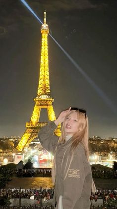 a woman standing in front of the eiffel tower at night with her hands on her head