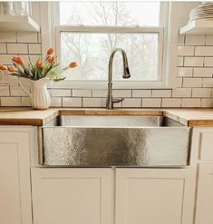 a kitchen sink sitting under a window next to a counter top with flowers in it