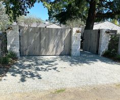 a driveway with a gate and trees in the back ground, surrounded by brick pavers