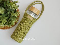 a green crocheted bag next to a potted plant on a white surface