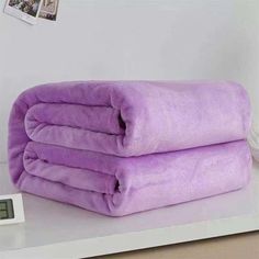 two purple towels stacked on top of each other next to a digital scale and alarm clock