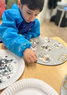 a young boy sitting at a table with paper plates on it and looking at pictures