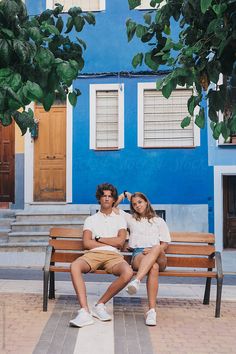 two people sitting on a bench in front of a blue building