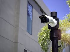 a security camera on top of a pole next to a building with palm trees in the background