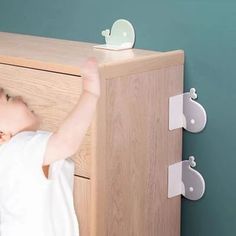 a small child reaching up to reach the top of a wooden cabinet with hooks on it