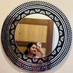 a woman taking a selfie in front of a round mirror with black and white designs on it