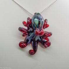 "This is the Red Blizzard Kracken. Made with a blood red glass with tiny white snowflakes all thru it. Beautiful Indigo and turquoise hood markings. Still approx 2.25\" across, formed in the torch and properly annealed in a digital kiln for durability, this one arrives safely wrapped and with your choice of a twisted Chinese silk necklace or a silver mini ball chain necklace, ready to give or keep. Handmade glass eye chip gives him such realistic eyes, you might want to keep him on his rope, jus Red Whimsical Jewelry For Gift, Whimsical Red Jewelry For Gift, Whimsical Red Jewelry For A Gift, Unique Red Glass Necklace, Handmade Red Necklaces For Collectors, Red Handmade Necklace For Collectors, Unique Red Necklace For Collectors, Glass Octopus, Realistic Eyes