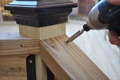 a person using a screwdriver to attach the top of a wooden fence post