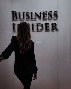 a woman is walking in front of the business insider logo on a glass wall with her hands out