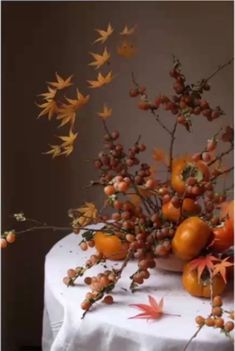 an arrangement of oranges and berries on a white tablecloth with autumn leaves in the background