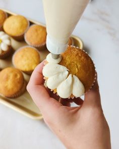 a person is holding a cupcake with icing on it and some muffins in the background