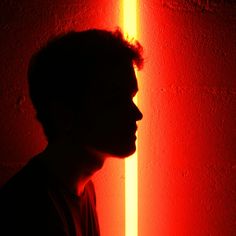 a man standing in front of a red and yellow wall with his head turned to the side