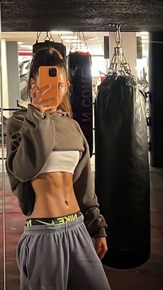 a woman taking a selfie in front of a punching bag with her cell phone