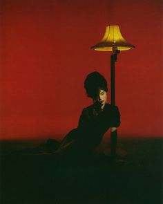 a woman sitting on the ground next to a lamp with a yellow shade over her head