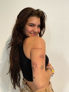 a woman with long hair and tattoos on her arm smiling at the camera while standing in front of a white wall