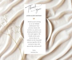 a thank card with a heart on it next to some flowers and a white sheet