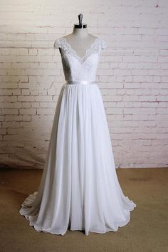 a white wedding dress on a mannequin stand in front of a brick wall