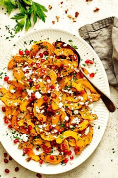 a white plate topped with squash and pomegranate covered in feta cheese