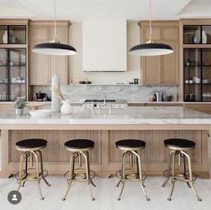 a kitchen with marble counter tops and stools in front of an island that has three lights hanging over it