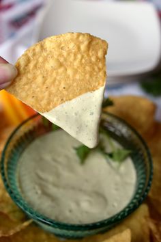 a hand holding a tortilla chip over a bowl of dip