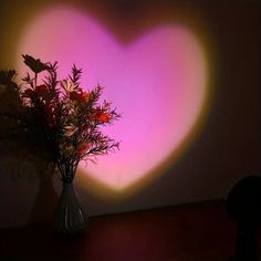 a vase filled with flowers sitting on top of a table next to a heart shaped wall