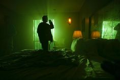 a person standing on a bed in a room with green light coming from the windows