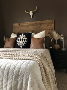 a bed with pillows, blankets and a cow skull on the wall above it's head