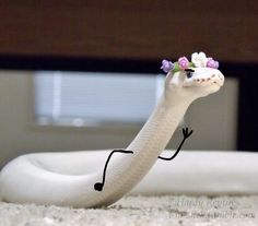 a white snake with purple flowers on its head and legs is in the middle of a bed