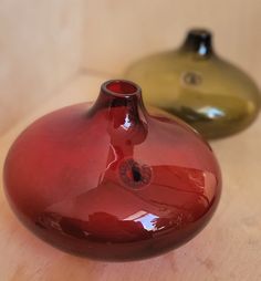 two small vases sitting on top of a wooden table next to each other in different colors