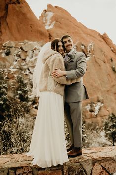 a bride and groom embracing each other in front of a rocky mountain backdrop with snow on the ground