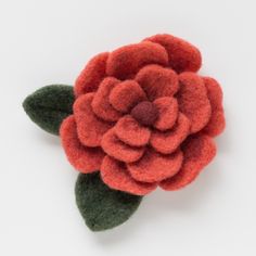 a red flower with green leaves is on a white surface in the shape of a brooch