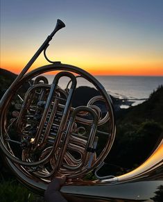 a person holding up a french horn in front of the ocean at sunset or sunrise