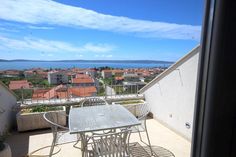 an outdoor table and chairs on a balcony overlooking the city with water in the background