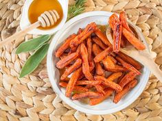 a white bowl filled with carrots next to a wooden spoon on top of a woven place mat