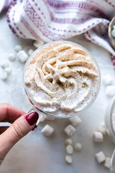 a hand holding a spoon with a drink in it and marshmallows scattered around