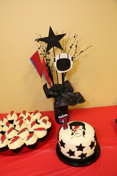 a table topped with cakes and cupcakes on top of a red table cloth