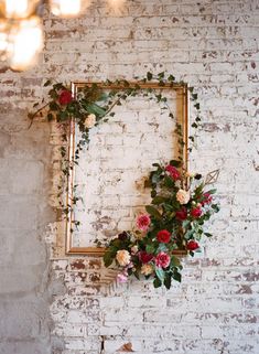 a white brick wall with a gold frame decorated with flowers and greenery on it