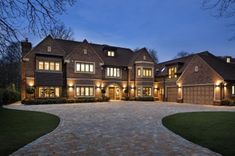 a large brick driveway leading to a two story house with lights on at night time