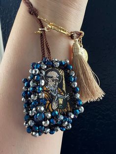 a hand with a beaded bracelet on it and a tasseled charm hanging from the wrist