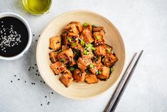 a bowl filled with tofu next to chopsticks and a cup of coffee