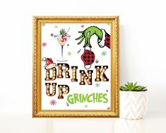 a framed poster with the words drink up grinies on it next to a potted plant