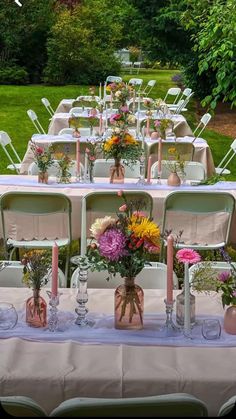 a long table is set up with flowers and vases on it for an outdoor wedding reception