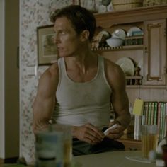 a man sitting at a kitchen table in front of a shelf with bottles on it