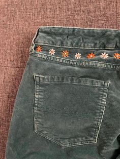 a pair of jeans with embroidered flowers on the back and side pockets, sitting on a brown surface